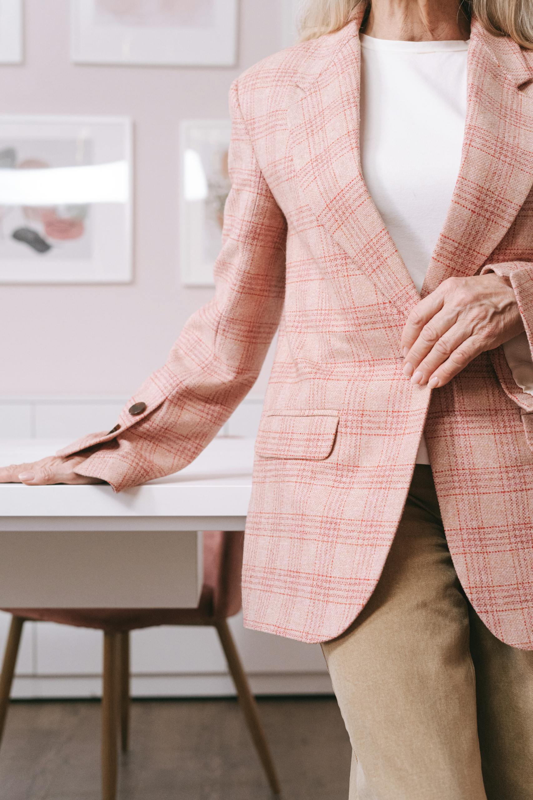 Stylish senior woman in pink plaid blazer standing in a modern home office setting.