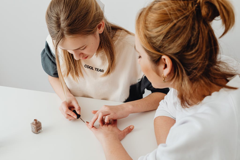 A young woman performs a manicure on another in a well-lit room, showcasing nail care and beauty.